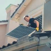 Man Wearing Safety Glasses and Gloves Holding Solar Panels on the Roof